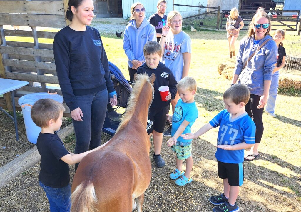 Cows and Coffee manager Kayla Hallmark, at left with her son Mason Higgins, 4, watch as Grayson Brady, 7, Theodore Hankerd, 4, and John Hankerd, 6, feed a Shetland pony at Asam Acres on Sept. 14. Looking on as the kids feed the pony are Ashley Brady, Sophia Friske, and Lauren Hankerd. (Photo by Erik Gable)