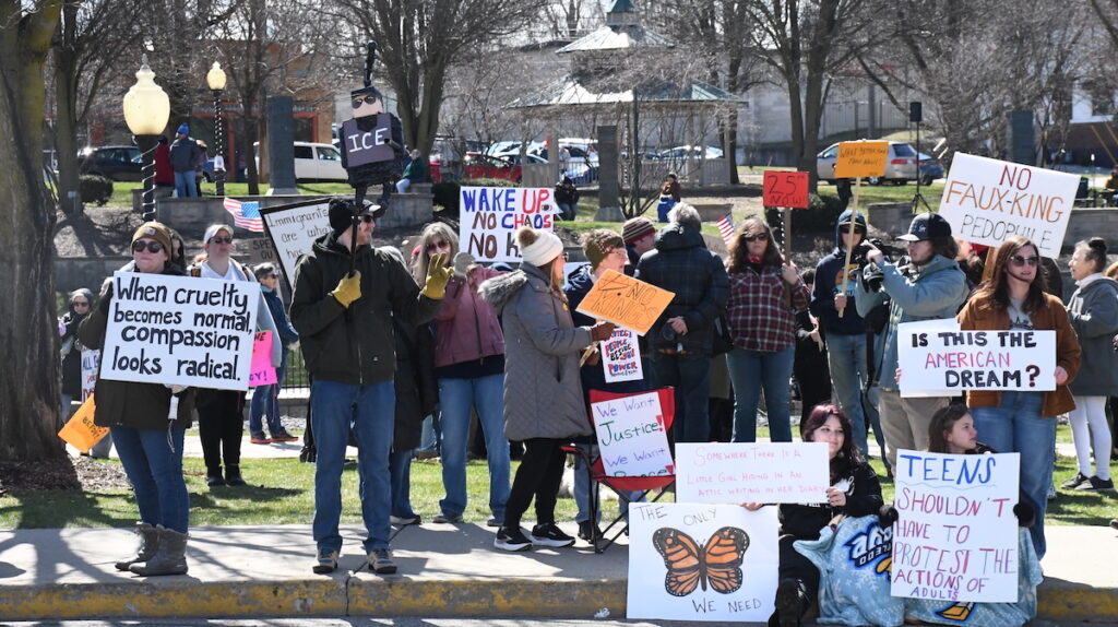 Protesters stand along West Maumee Street at the edge of Adrian's Comstock Park during a demonstration against the Trump administration on March 28.