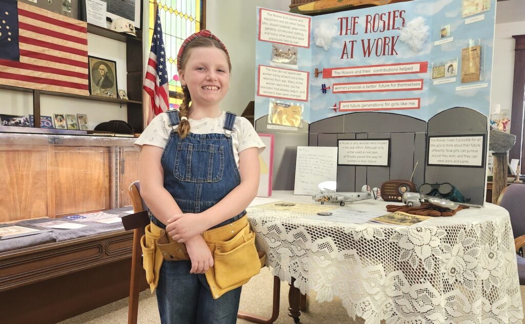 Annabelle Buechele-Beasecker is pictured with her project, “The Rosies at Work,” from this year’s Michigan History Day competition. (Photo by Erik Gable)