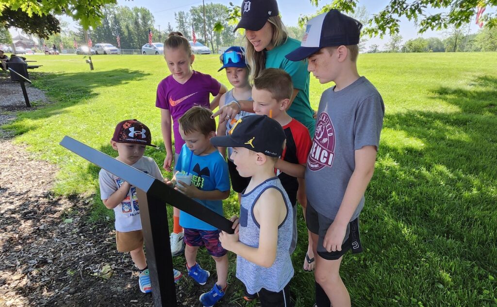 Vandria Erskin, along with her children and some friends, looks at one of the panels in the newly installed story walk at Morenci’s Wakefield Park. Pictured from left to right are Truett Erskin, Lyden Sarnac, Brooks Borton, Honor Erskin, Dawson Erskin, Kyden Borton, and Grayson Erskin. (Photo by Erik Gable/Lenawee Voice)