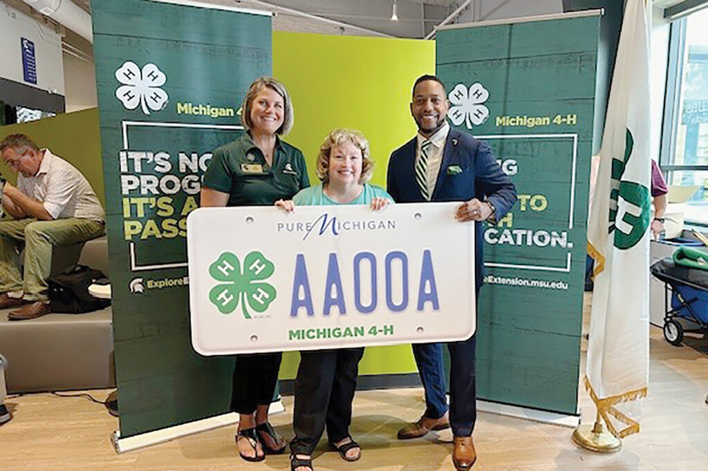 Michigan 4-H leader Jodi Schulz, State Rep. Reggie Miller, and MSU Extension Director Quentin Tyler hold up a draft 4-H license plate at an Aug. 15 event in Van Buren Township.