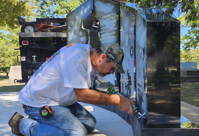 Stan Adams caulks the base of the new military monument on Sept. 17 in Adrian’s Oakwood Cemetery. The memorial was donated by Adrian Monument.