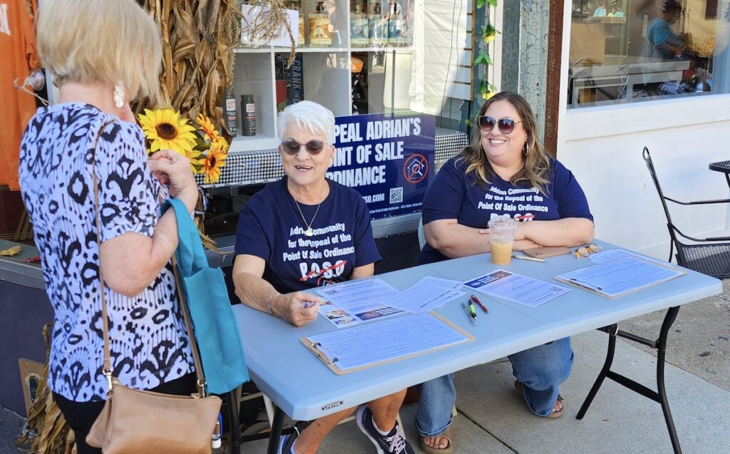 Diana Faust and Carrie Smith, both part of the petition drive to overturn the city of Adrian’s point-of-sale real estate inspection ordinance, talk with passersby at the Artalicious festival in downtown Adrian on Sept. 21.