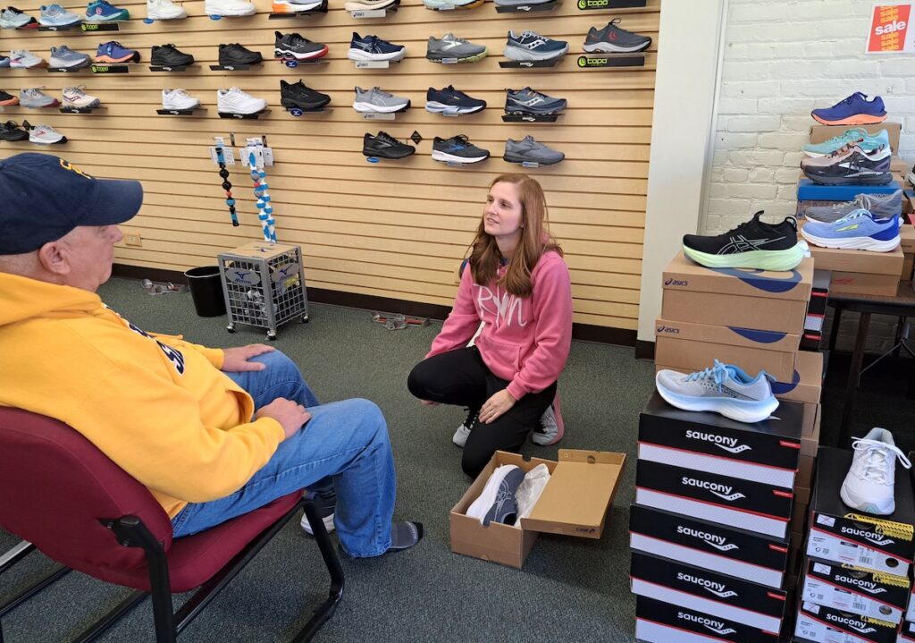 Rachel Miller demonstrates a shoe fitting with Tim Bauer at Running with E’s in downtown Adrian.