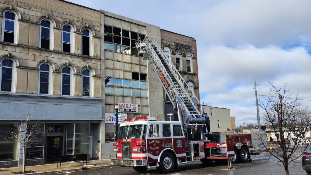 The Adrian Fire Department remained on the scene Sunday morning. Here, a firefighter on an aerial truck clears broken glass from windows.