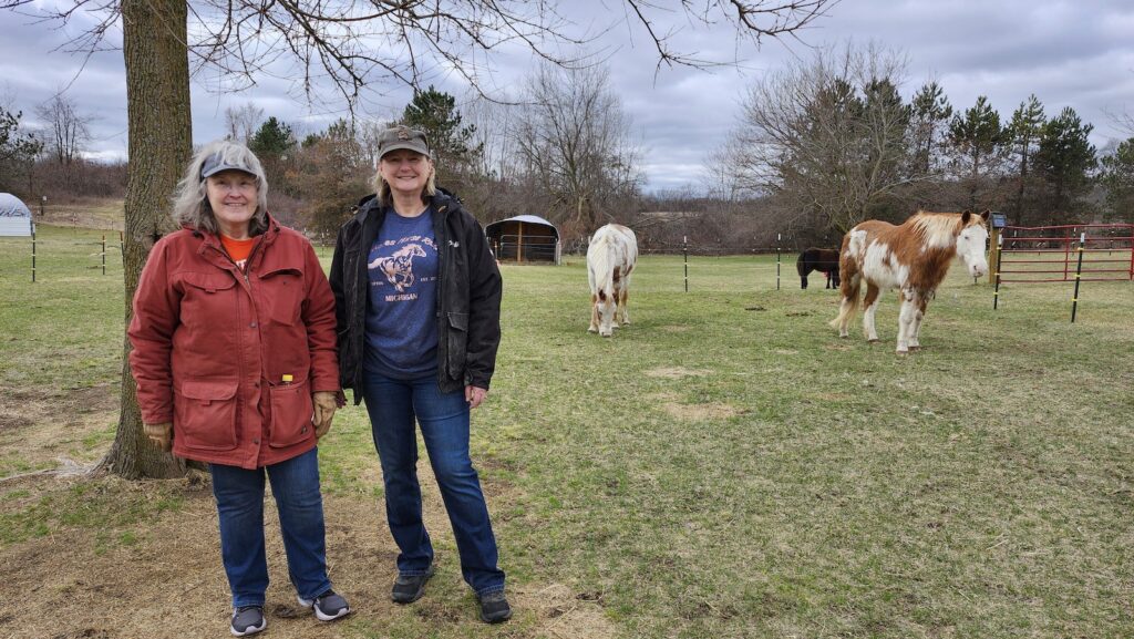 Sherry Duberville and Michelle Wild of Wild Acres Horse Rescue are pictured at the rescue’s Raisin Township location. The three horses who currently live at the facility — G.W., Mattie, and Harley — are in the background.