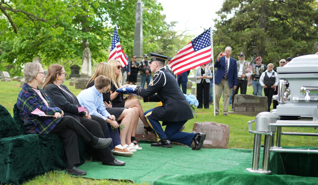 A pallbearer presents the American flag that had been draped over Staff Sgt. Ralph Mourer's casket to his granddaughter, Laura Spolsky, as her daughter Kailyn and son Connor look on. Next to Connor is Spolsky's mother, JoAnne Mourer of Adrian, who married Ralph Mourer's son, Victor. At left is Victor's half-sister, Peggy Ziegler. (Photo by Lad Strayer)
