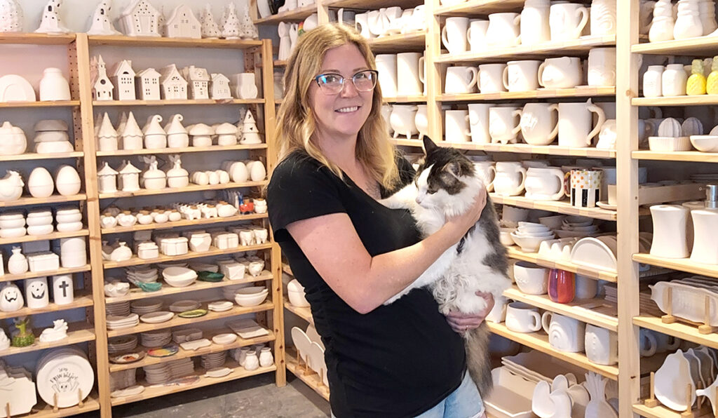Katie Flowers, owner of Clay it Forward, is pictured inside her new drop-in art studio with Kresnick, the store cat. Clay it Forward offers drop-in art experiences in downtown Tecumseh. (Photo by Julie C. Clemes)