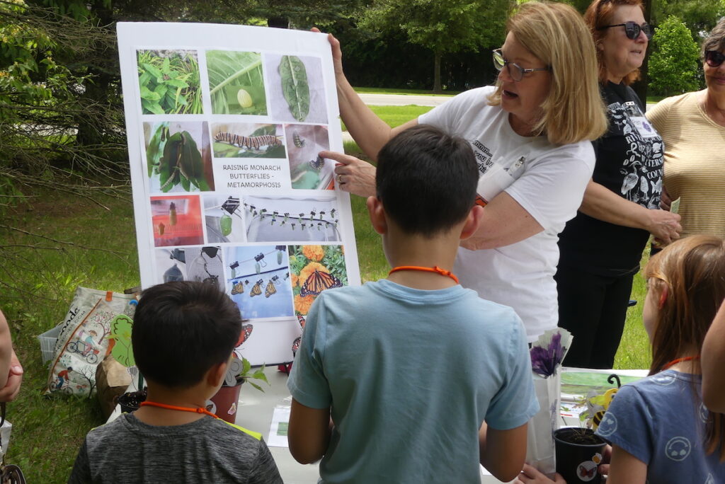Children, hands still grubby from potting plants, listen to a presenter sharing information about how to support native pollinators like monarch butterflies. (Photo by Kadi Franson)