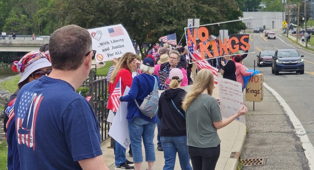 A large "No kings" banner and a sign quoting Leviticus 19:33 are displayed by demonstrators along West Maumee Street on June 14.
