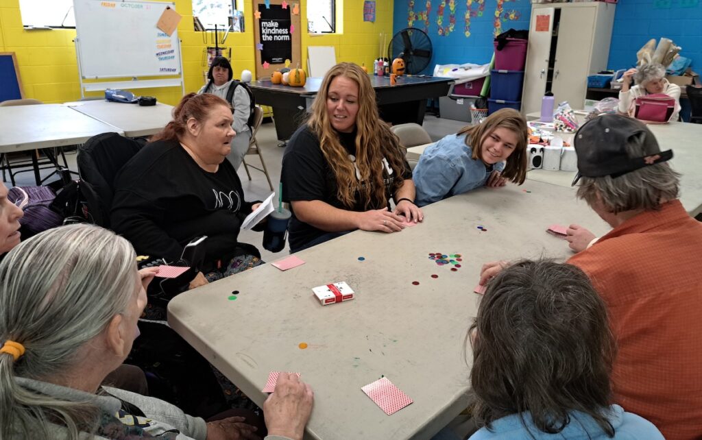 Katie O'Hotzke, the HOPE Community Center's new executive director, learns how to play a card game from some of the center's members.