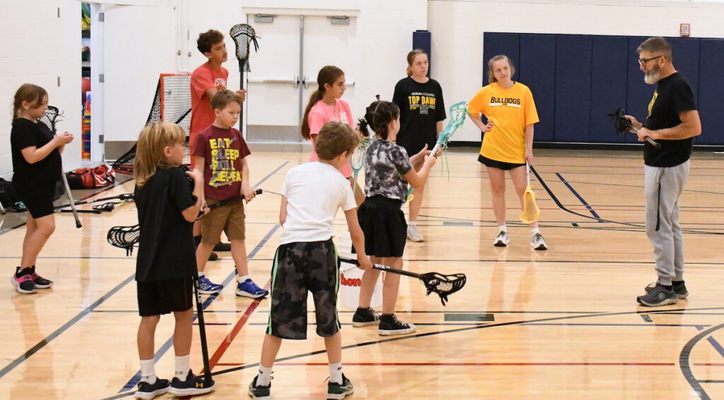 Carl Lewandoski, right, assisted by Adrian College lacrosse players and twin sisters Grace (left) and Avah Holland, teaches a Lacrosse Fundamentals clinic on Sept. 22 at the Frank & Shirley Dick Family YMCA. (Photos by Erik Gable)