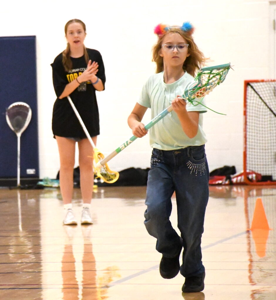 Adrian College lacrosse player Grace Holland cheers as Carolina Lopez practices running while cradling the ball.