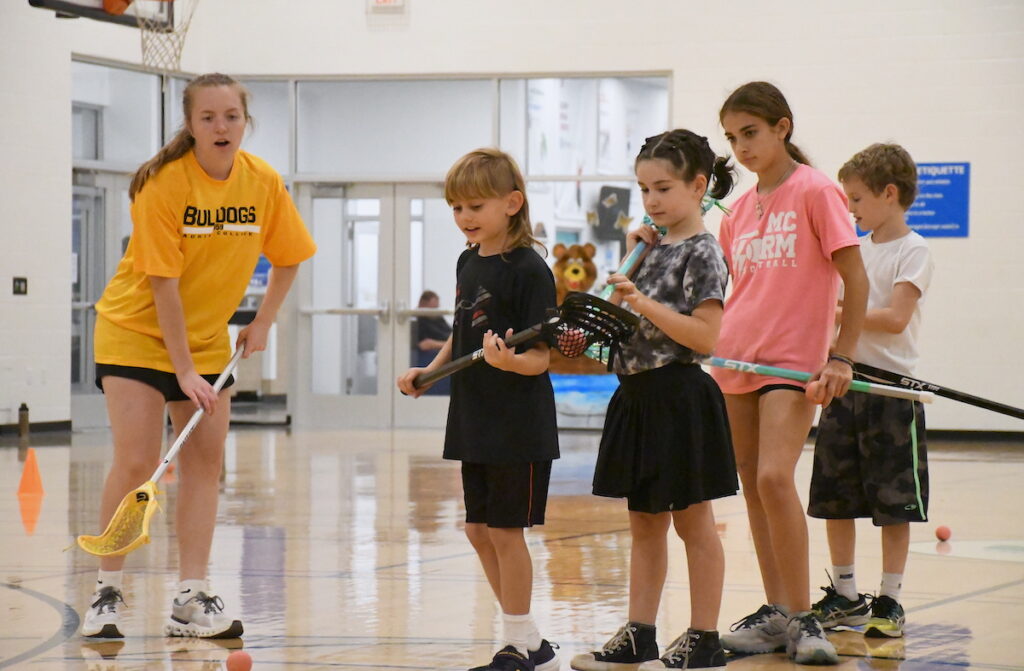 Avah Holland coaches Finley Staten, Lyla Ebeling, Emma Santos, and Finn Almes in throwing technique during a Lacrosse Fundamentals clinic offered by Lenawee Youth Lacrosse at the Frank & Shirley Dick Family YMCA.