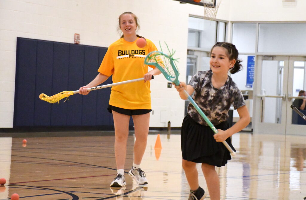 Lyla Ebeling practices her throwing technique during a Lenawee Youth Lacrosse fundamentals clinic while Avah Holland, a Tecumseh High School graduate and Adrian College lacrosse player, watches.