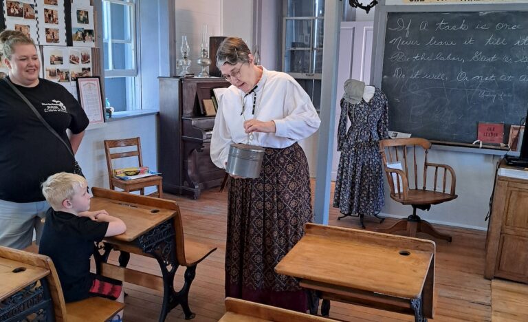Sally Freese, in period attire as a schoolteacher, shows visitors a lunchpail typical of what might have been carried by a student at the Wooden Stone School. (Photos by Arlene Bachanov)
