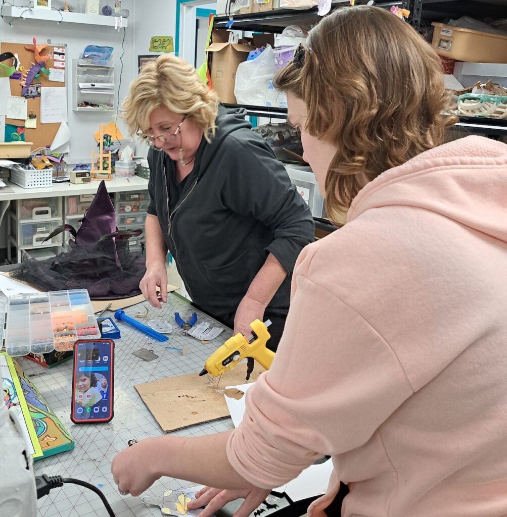 Taina Mantey, the ACA’s youth programming director, helps a student finish her piece using a glue gun. Mantey is retired from Britton Deerfield schools and now manages youth programs at the Adrian Center for the Arts. (Photo by Arlene Bachanov)