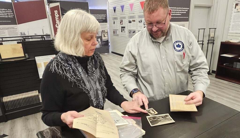 Sheri Reeves Bleam shows Bob Behnke a collection of photographs and documents belonging to her mother, an Austrian citizen who lived under the Nazi regime. The papers are part of a temporary exhibit about the Holocaust that will be displayed at the Gallery of Shops in downtown Adrian through April 26. (Photo by Erik Gable)