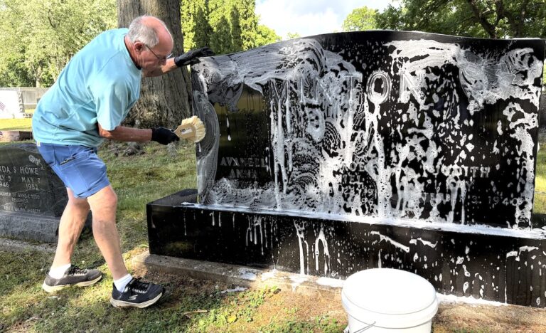 Bill Camp works on cleaning a headstone at Maple Grove Cemetery in Hudson. He was inspired to start his business, The Monument Man, by seeing headstones that were weathered or darkened by moss and feeling that something should be done to preserve the names they bore. (Photo by Renee Lapham Collins)