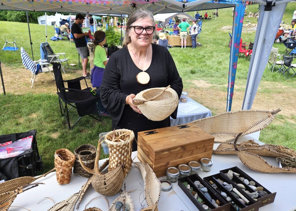 Artist Ruth Rushlow, one of the many vendors at the Great Lakes Foragers Gathering, stands behind a display of her hand-woven basketry. (Photos by Kadi Franson)