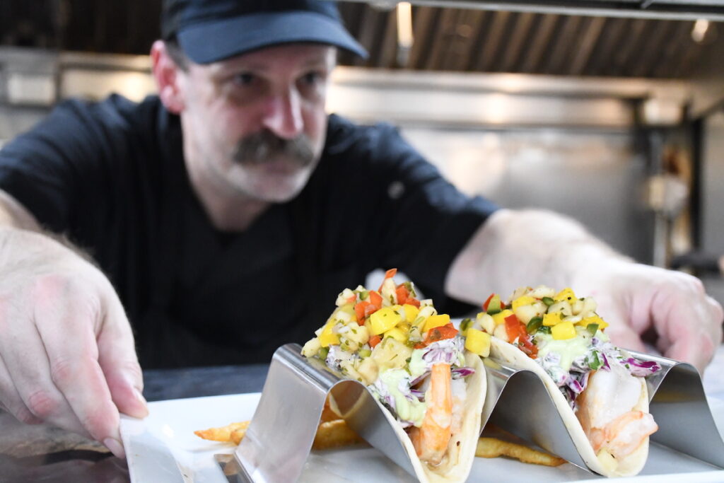 Chef Justin Hill pushes out an order of shrimp tacos at the July 17 soft opening of The Stable in Blissfield.