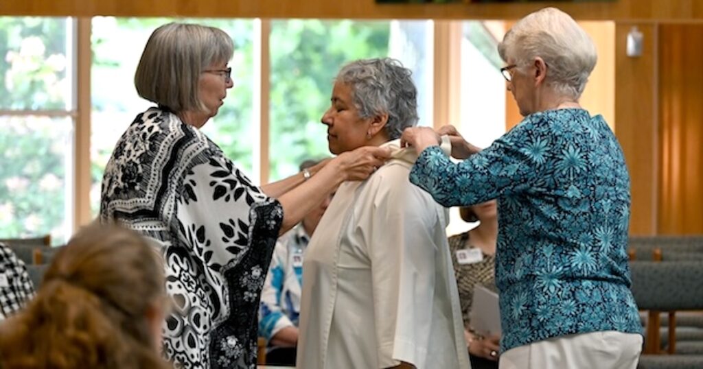 Sister Sara Fairbanks, left, and Sister Tarianne DeYonker, right, help to clothe Sister Elizabeth Guerrero in a preaching garment as part of her reception into the novitiate.