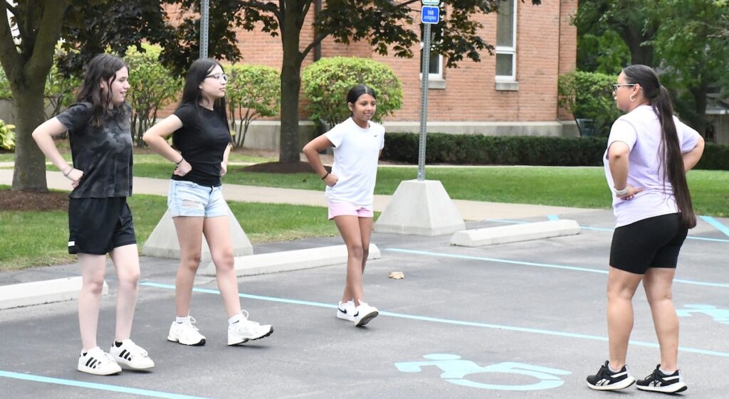 Teresa Gutierrez teaches a dance to Izabel Morgan, Juliana Ramirez, and Ameera Torres during a practice on Aug. 21 outside the St. Joseph campus of Holy Family Parish in Adrian.