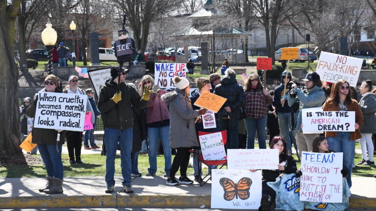 Protesters stand along West Maumee Street at the edge of Adrian's Comstock Park during a demonstration against the Trump administration on March 28.
