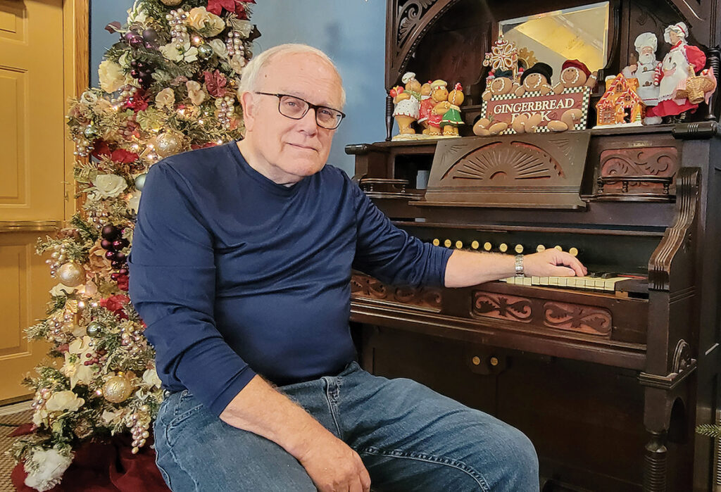 In his profession as a pastor, Bill Van Valkenburg has presided over many funerals. In his work at Anderson-Marry Funeral Home, he brings beauty to hard times by decorating an extensive display of Christmas trees. He’s pictured here at the antique pump organ at the funeral home, which still works and which Van Valkenburg can play.